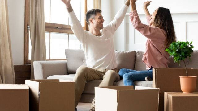 Two people surrounded by boxes, having just moved in together, cheering and happy